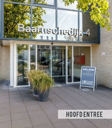 Hoofdentree van het gebouw aan de Baarnsche Dijk 4 met een welkomstbord en planten bij de ingang.